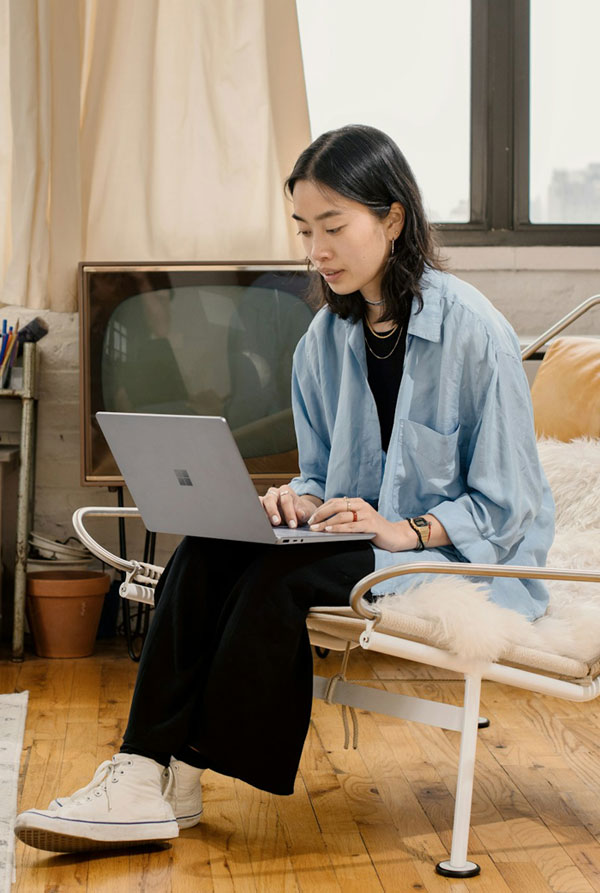 Woman studying on laptop while sitting on a chair with fluffy cushions